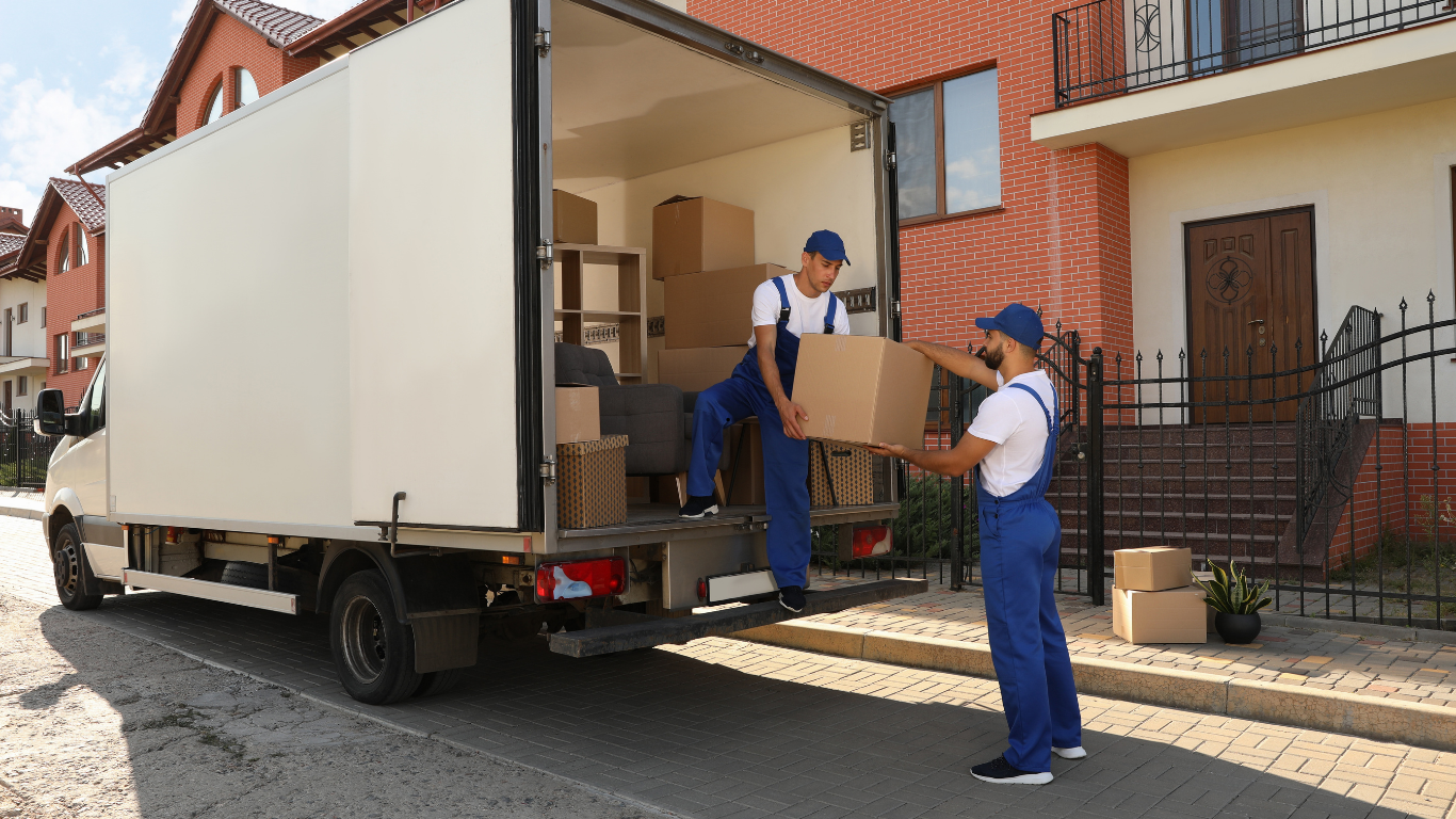 Two Ahmed Man With Van movers unloading boxes and furniture from the back of a removals van outside a house